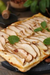 Photo of Delicious puff pastry tart with pears, almond and mint on wooden table, closeup