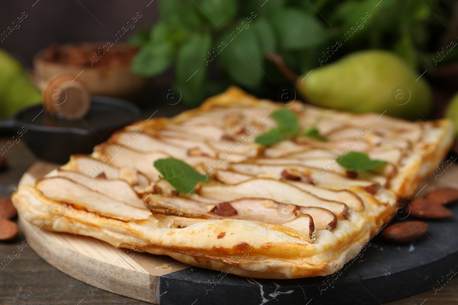 Photo of Delicious puff pastry tart with pears, almond and mint on wooden table, closeup