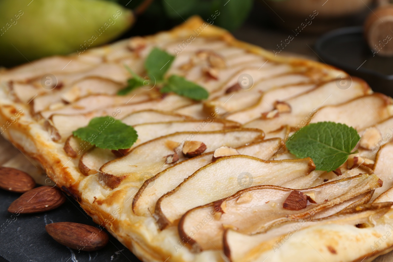 Photo of Delicious puff pastry tart with pears, almond and mint on table, closeup