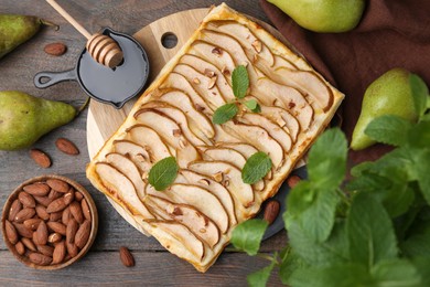 Photo of Delicious puff pastry tart with pears, almond and mint on wooden table, flat lay