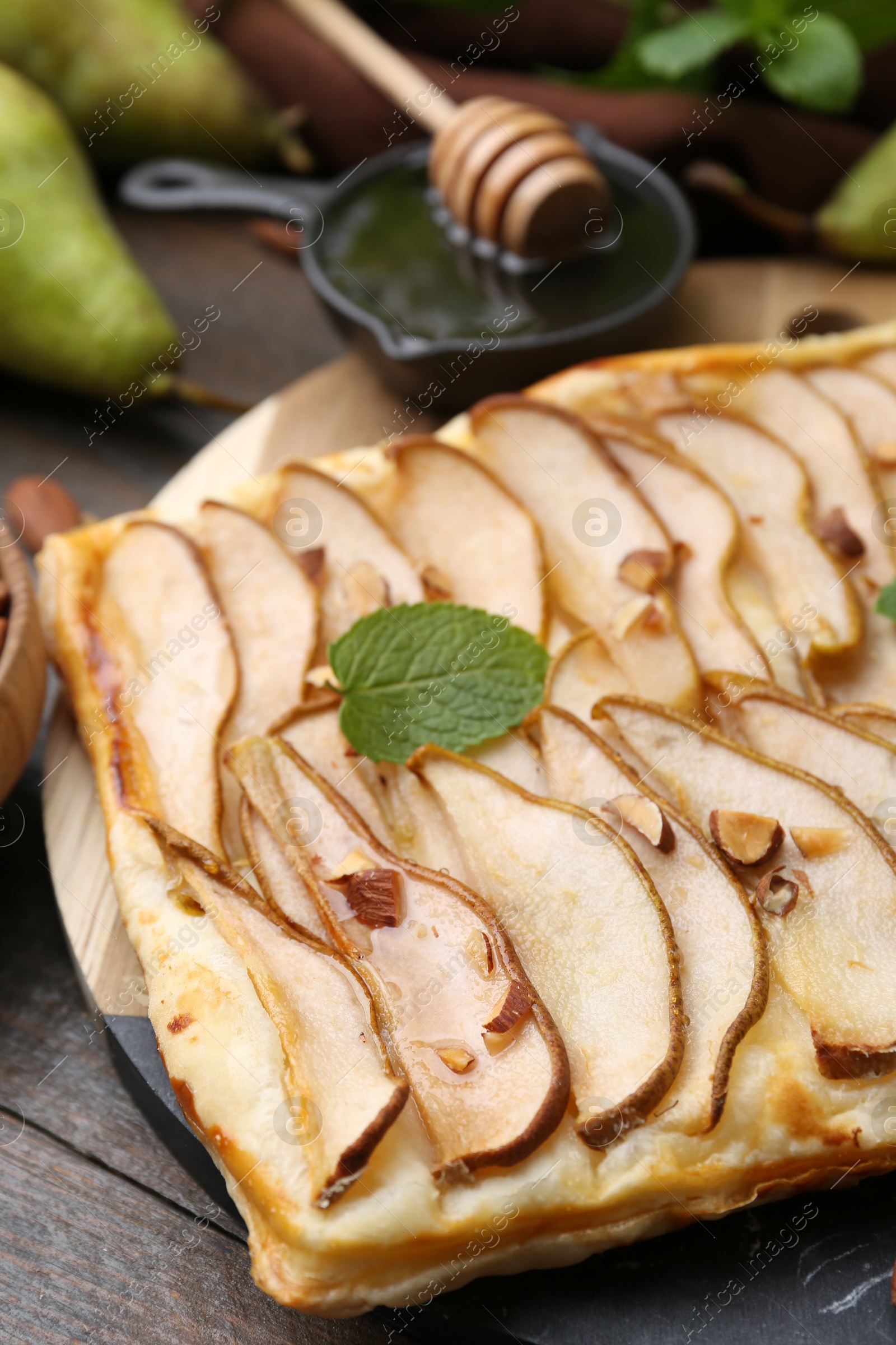 Photo of Delicious puff pastry tart with pears, almond and mint on wooden table, closeup