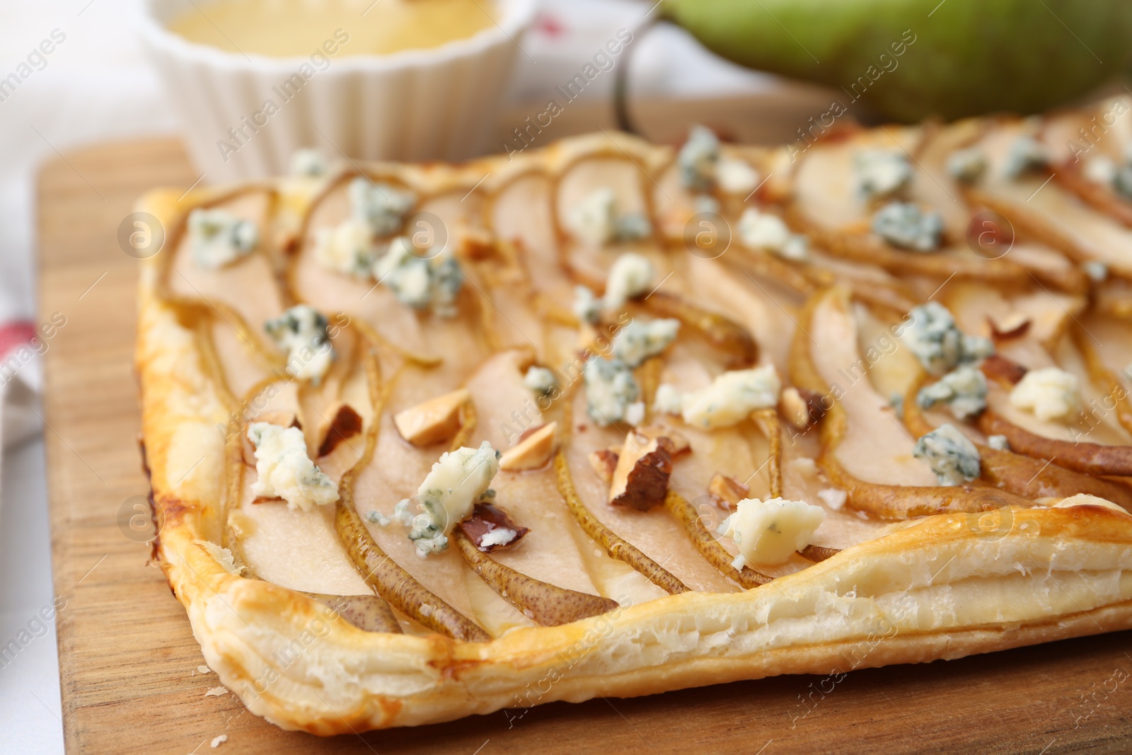 Photo of Delicious puff pastry tart with pears, almond and blue cheese on wooden board, closeup