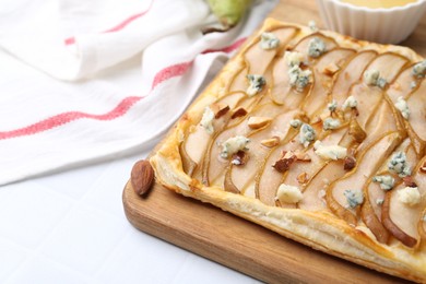 Delicious puff pastry tart with pears, almond and blue cheese on light tiled table, closeup