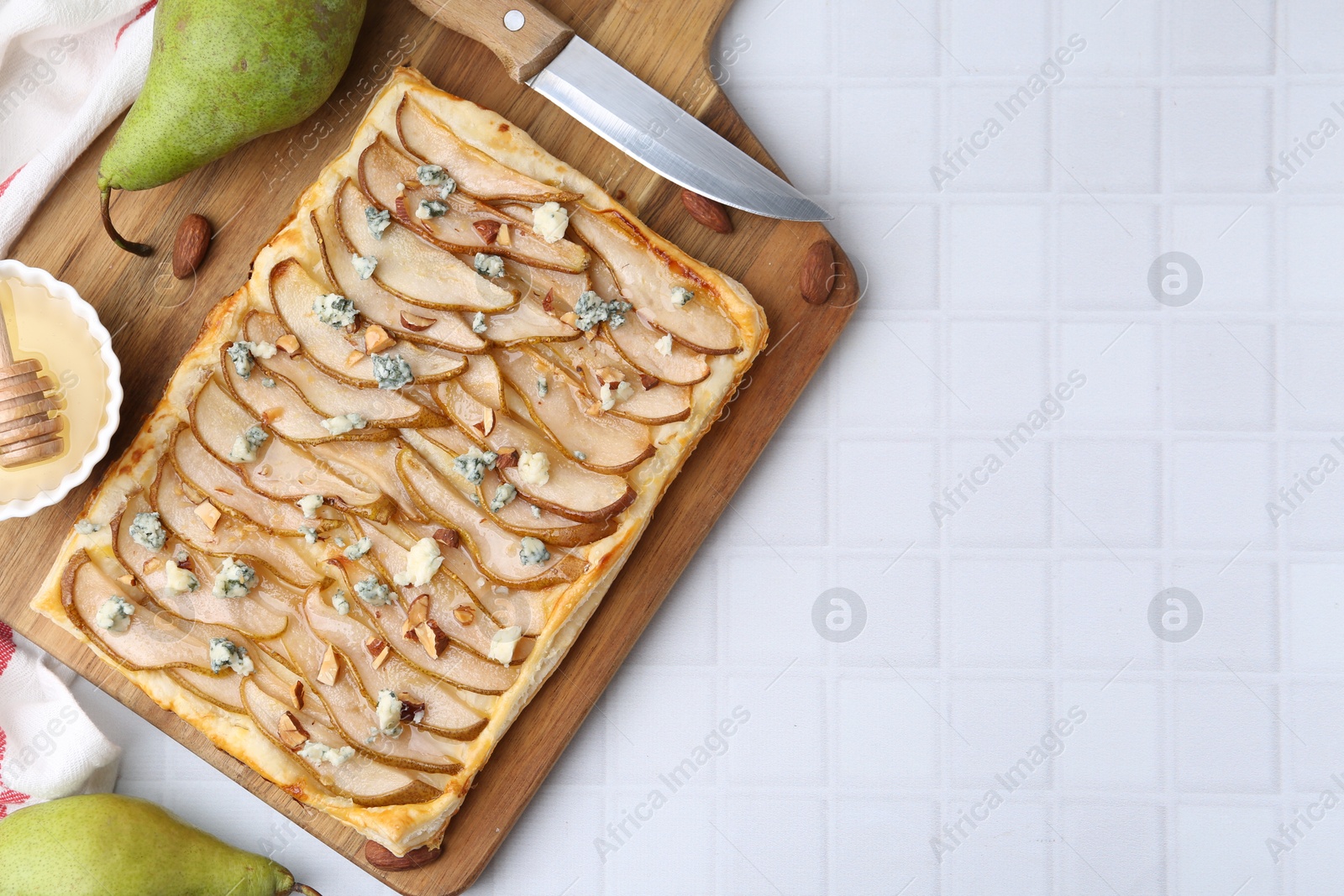 Photo of Delicious puff pastry tart with pears, almond, honey and blue cheese on light tiled table, flat lay. Space for text