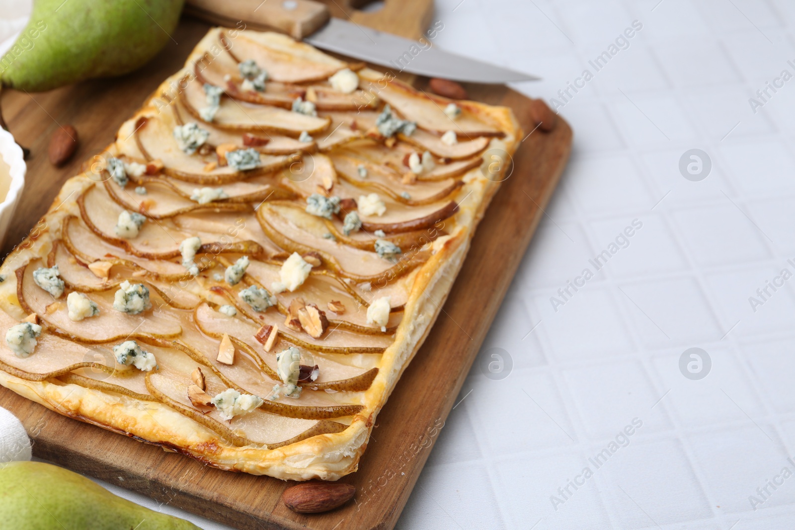 Photo of Delicious puff pastry tart with pears, almond and blue cheese on light tiled table, closeup. Space for text