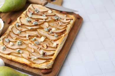 Photo of Delicious puff pastry tart with pears, almond and blue cheese on light tiled table, closeup. Space for text