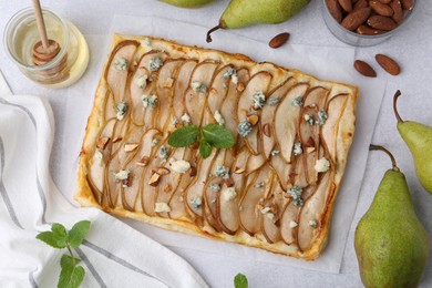 Photo of Delicious puff pastry tart with pears, almond, mint and blue cheese on light table, flat lay