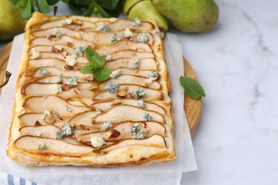 Delicious puff pastry tart with pears, almond, mint and blue cheese on white marble table, closeup. Space for text