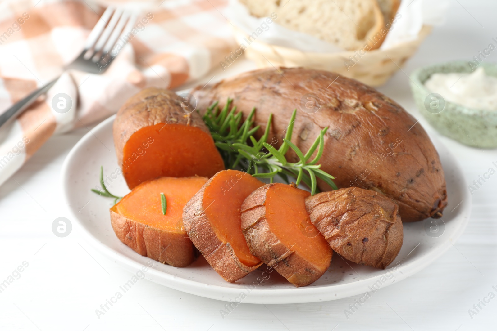 Photo of Tasty cooked sweet potatoes and rosemary on white table, closeup