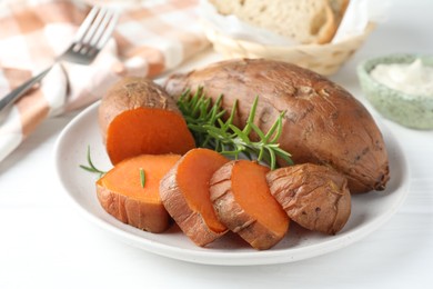 Photo of Tasty cooked sweet potatoes and rosemary on white table, closeup