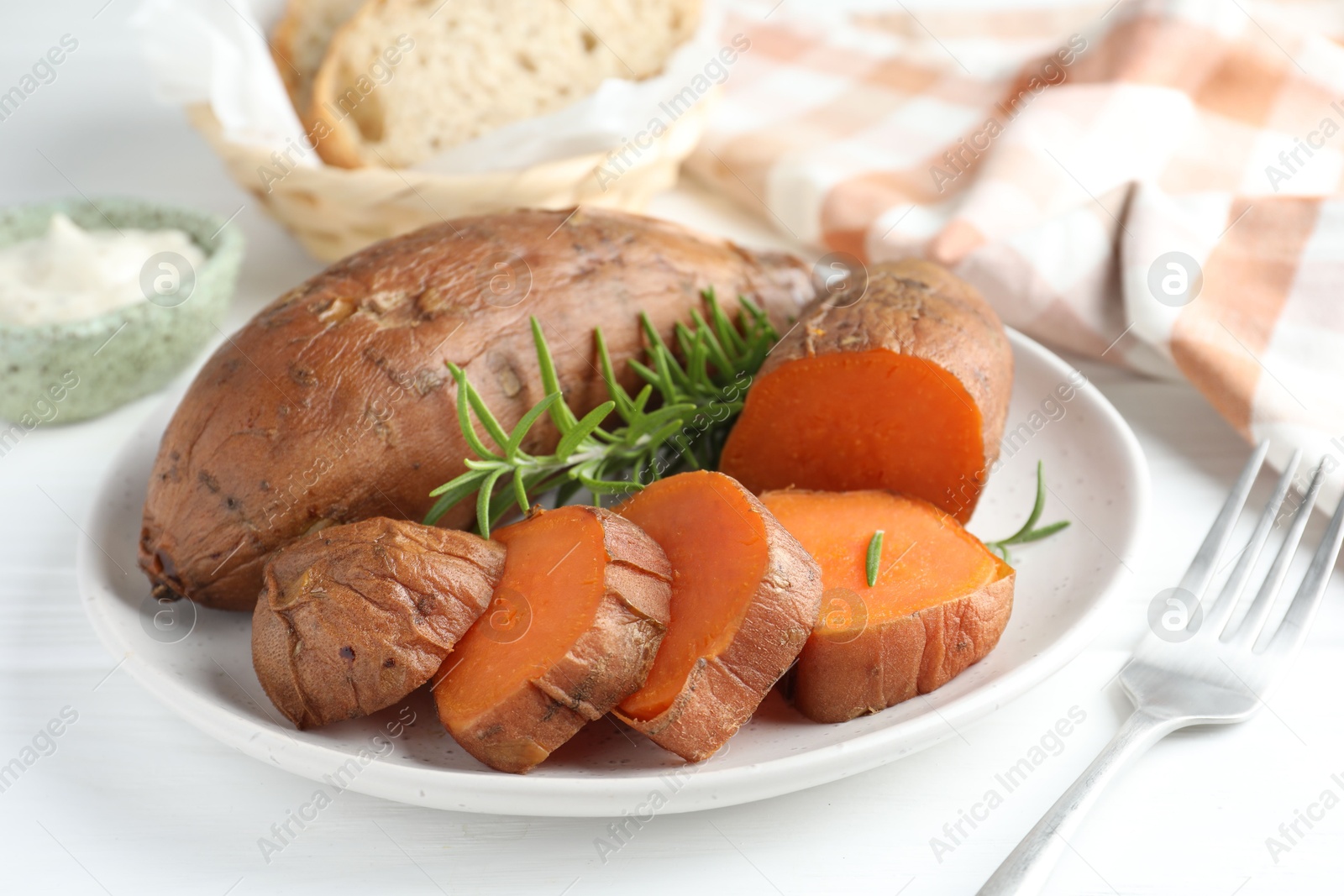 Photo of Tasty cooked sweet potatoes and rosemary on white table, closeup