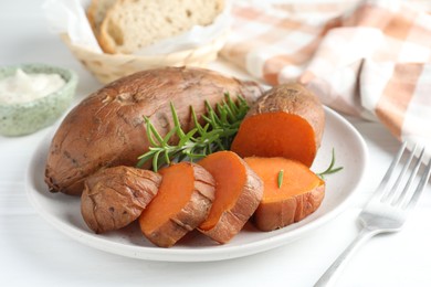 Photo of Tasty cooked sweet potatoes and rosemary on white table, closeup