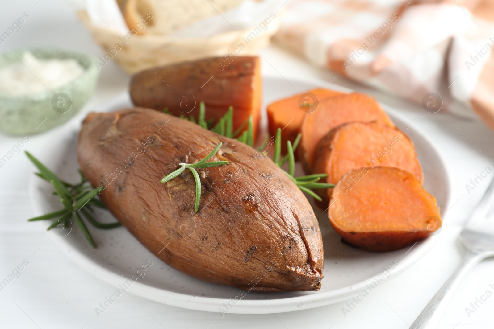 Photo of Tasty cooked sweet potatoes and rosemary on white table, closeup