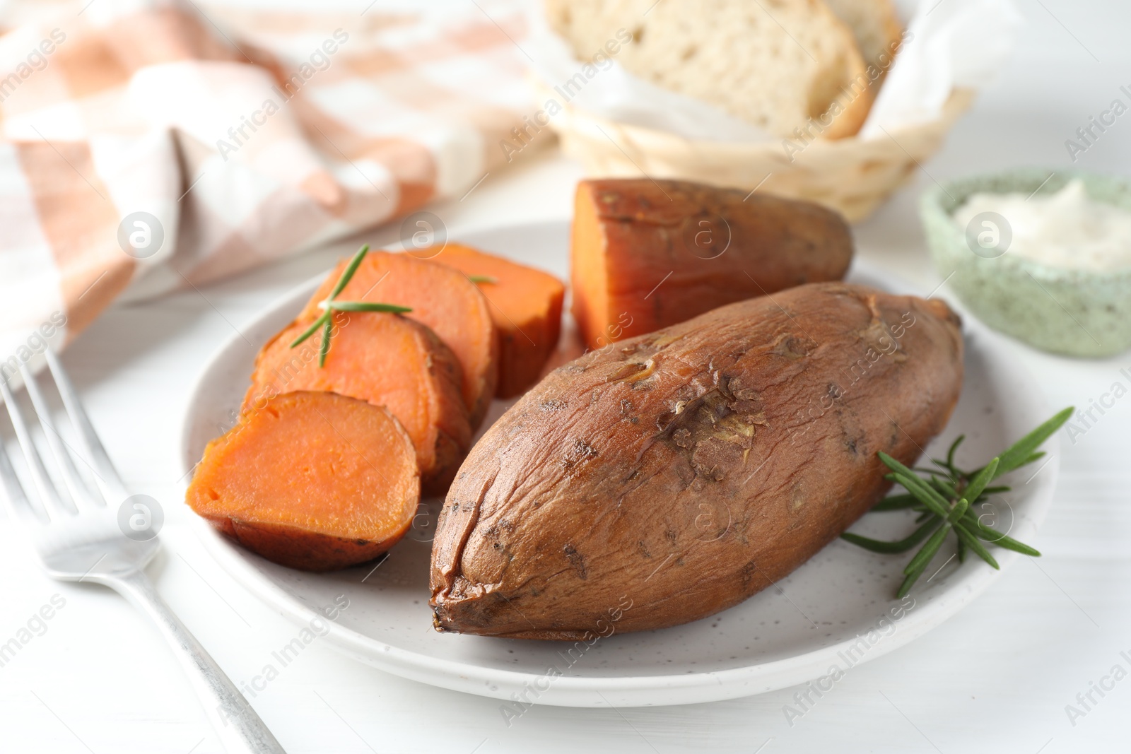 Photo of Tasty cooked sweet potatoes and rosemary on white table, closeup