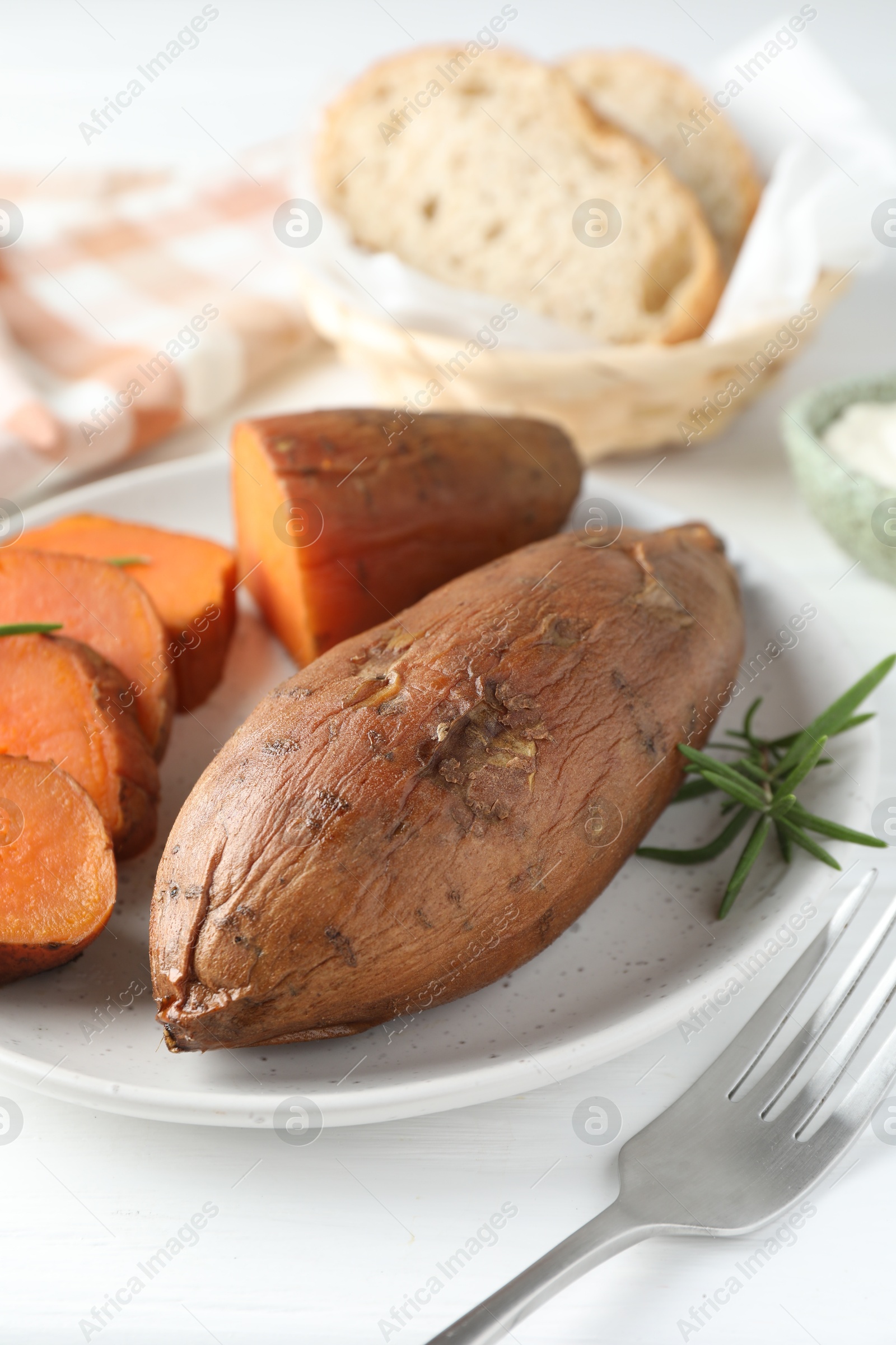 Photo of Tasty cooked sweet potatoes and rosemary on white table, closeup