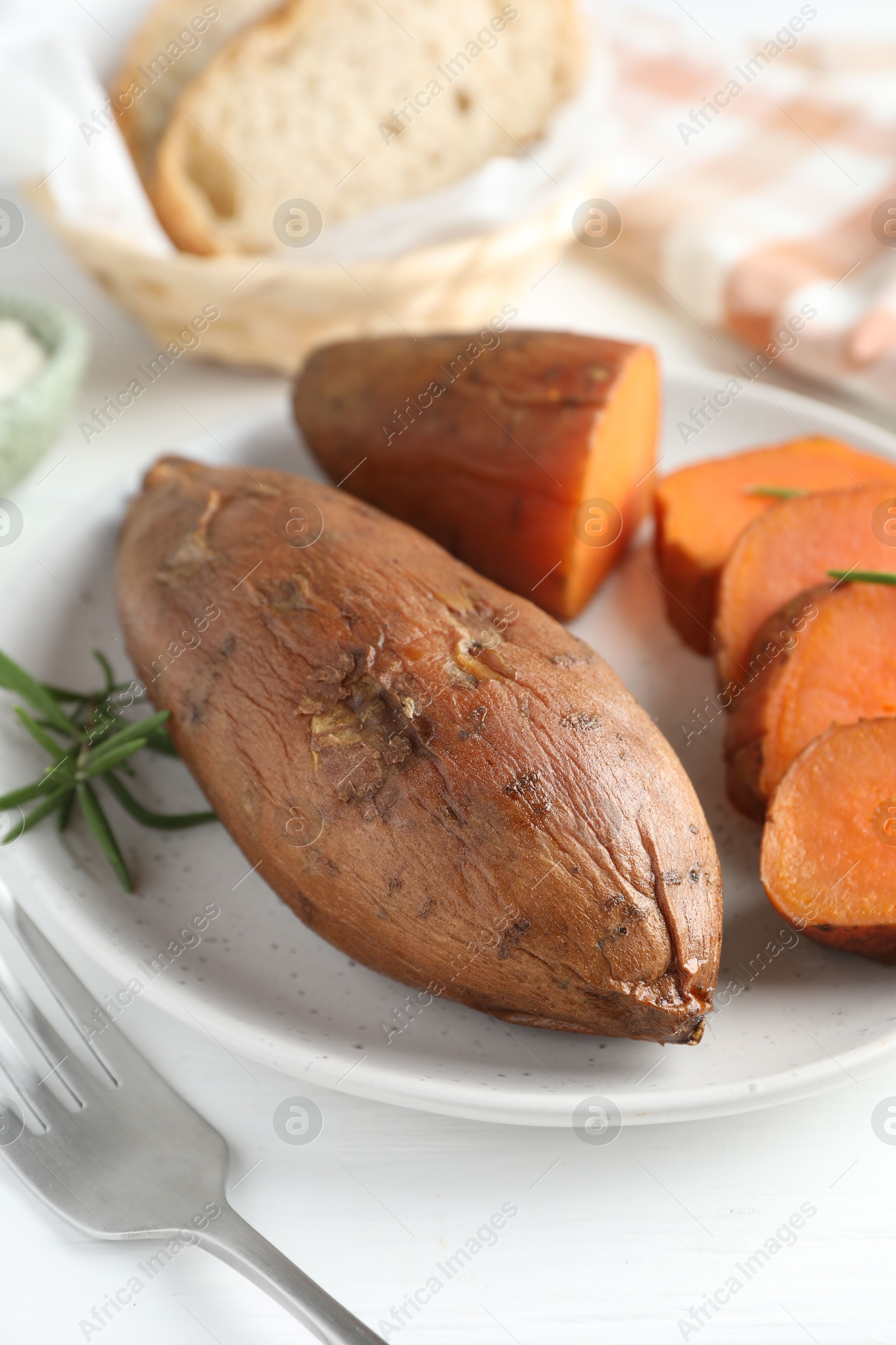 Photo of Tasty cooked sweet potatoes and rosemary on white table, closeup