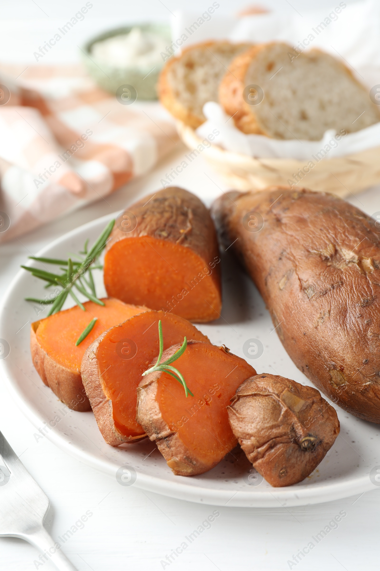 Photo of Tasty cooked sweet potatoes and rosemary on white table, closeup