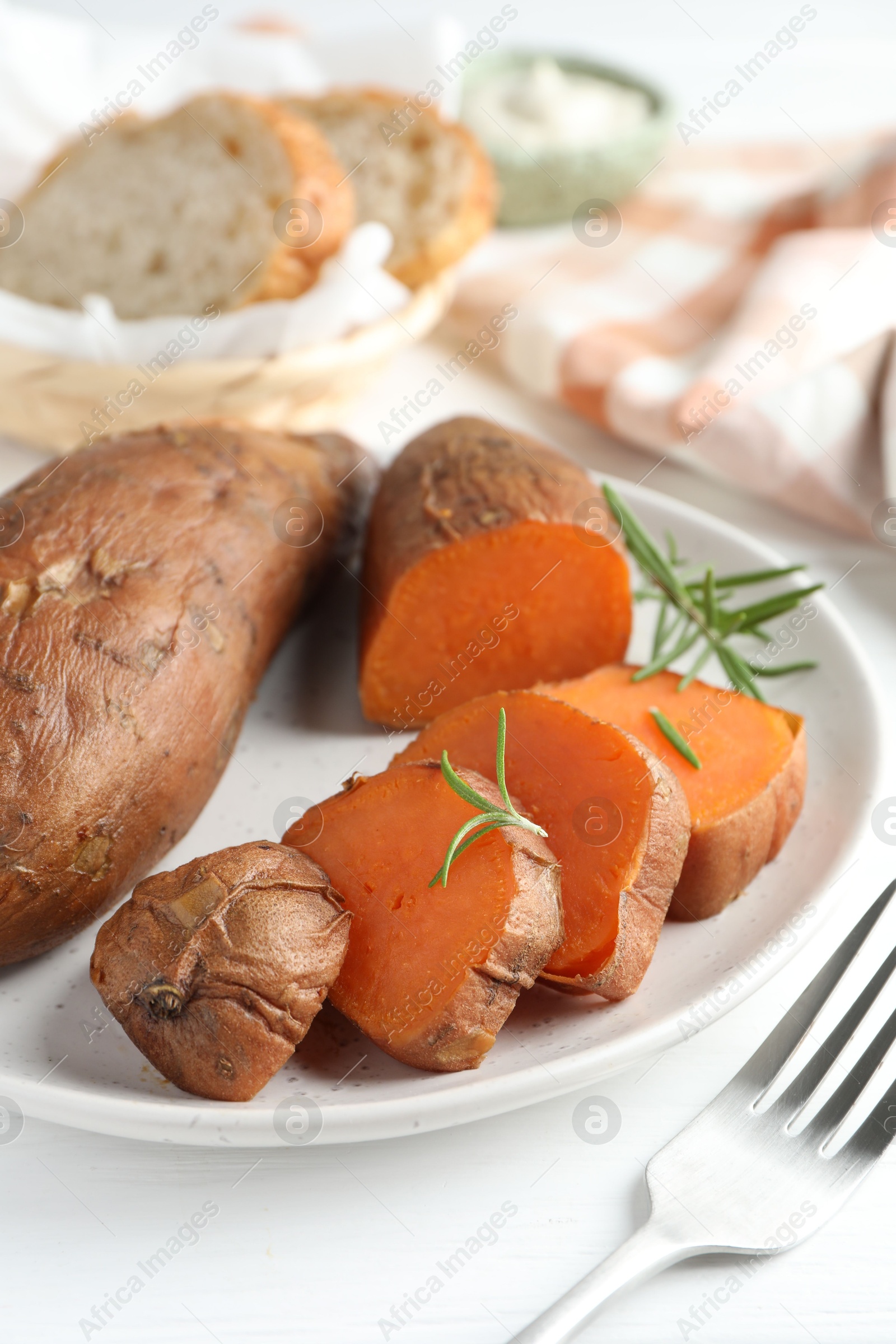 Photo of Tasty cooked sweet potatoes and rosemary on white table, closeup