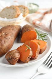 Photo of Tasty cooked sweet potatoes and rosemary on white table, closeup