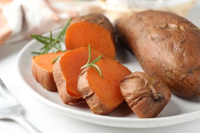 Photo of Tasty cooked sweet potatoes and rosemary on table, closeup