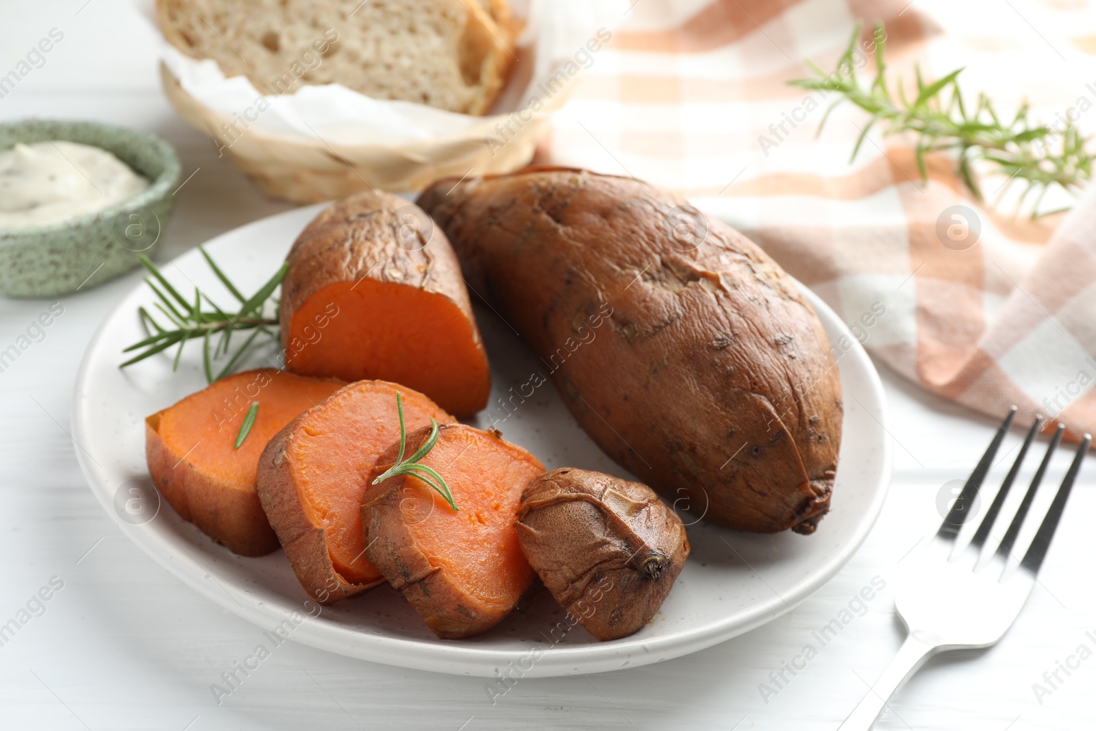 Photo of Tasty cooked sweet potatoes served with rosemary on white wooden table, closeup