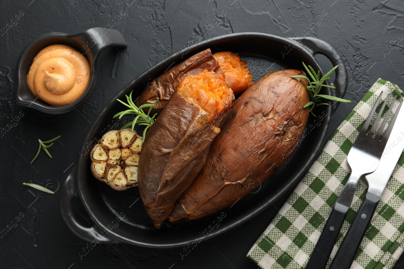 Photo of Tasty cooked sweet potatoes served with rosemary and sauce on black table, top view