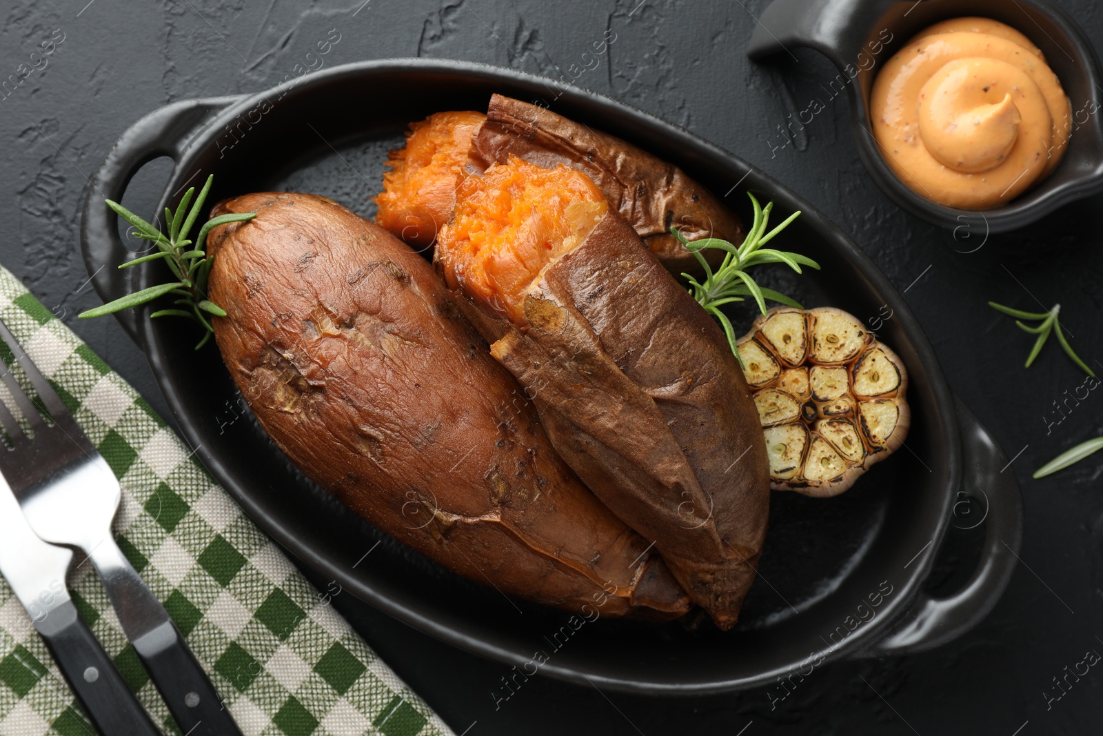 Photo of Tasty cooked sweet potatoes served with rosemary and sauce on black table, top view