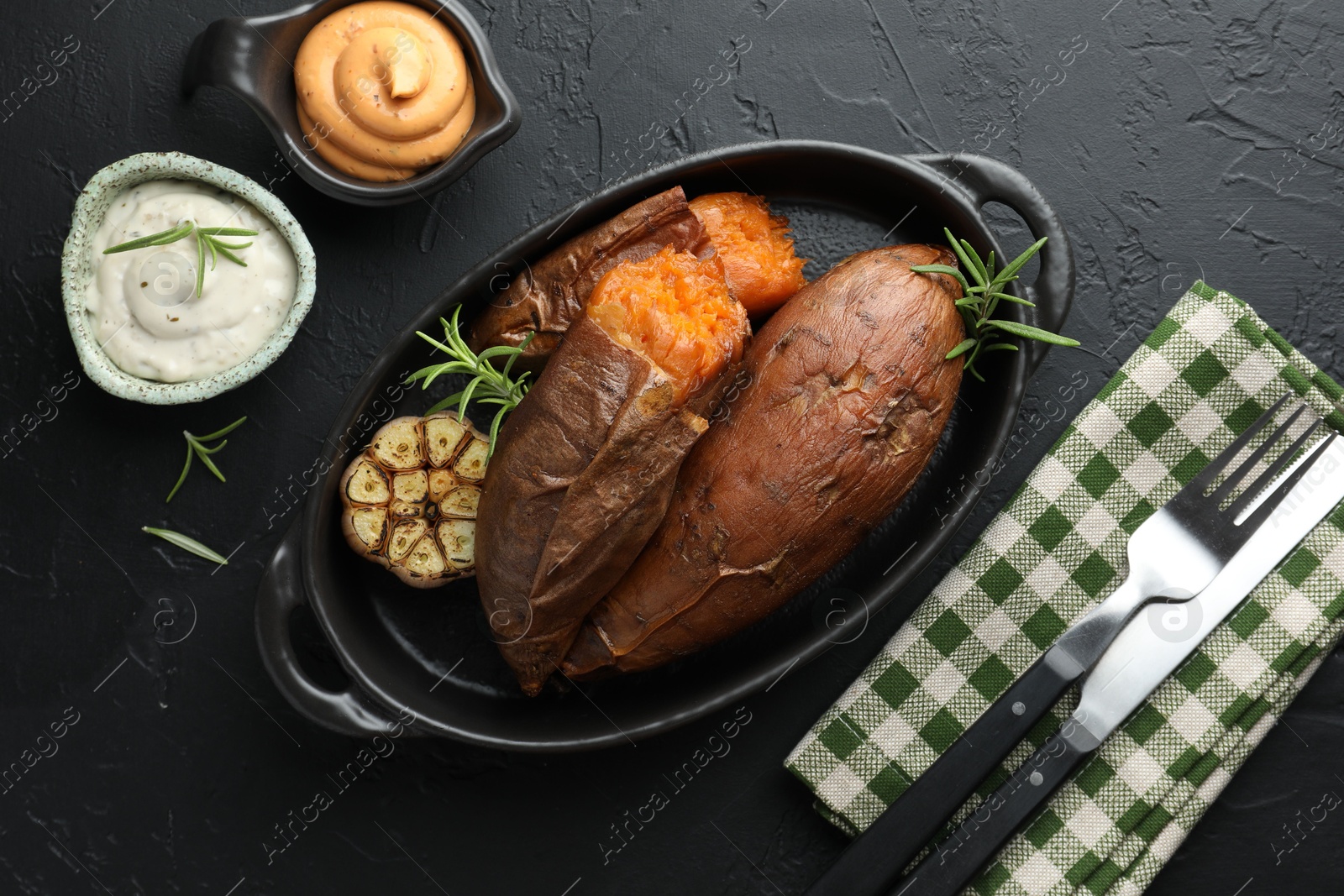 Photo of Tasty cooked sweet potatoes served with rosemary and sauces on black table, top view