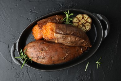 Photo of Tasty cooked sweet potatoes, rosemary and garlic on black table, top view