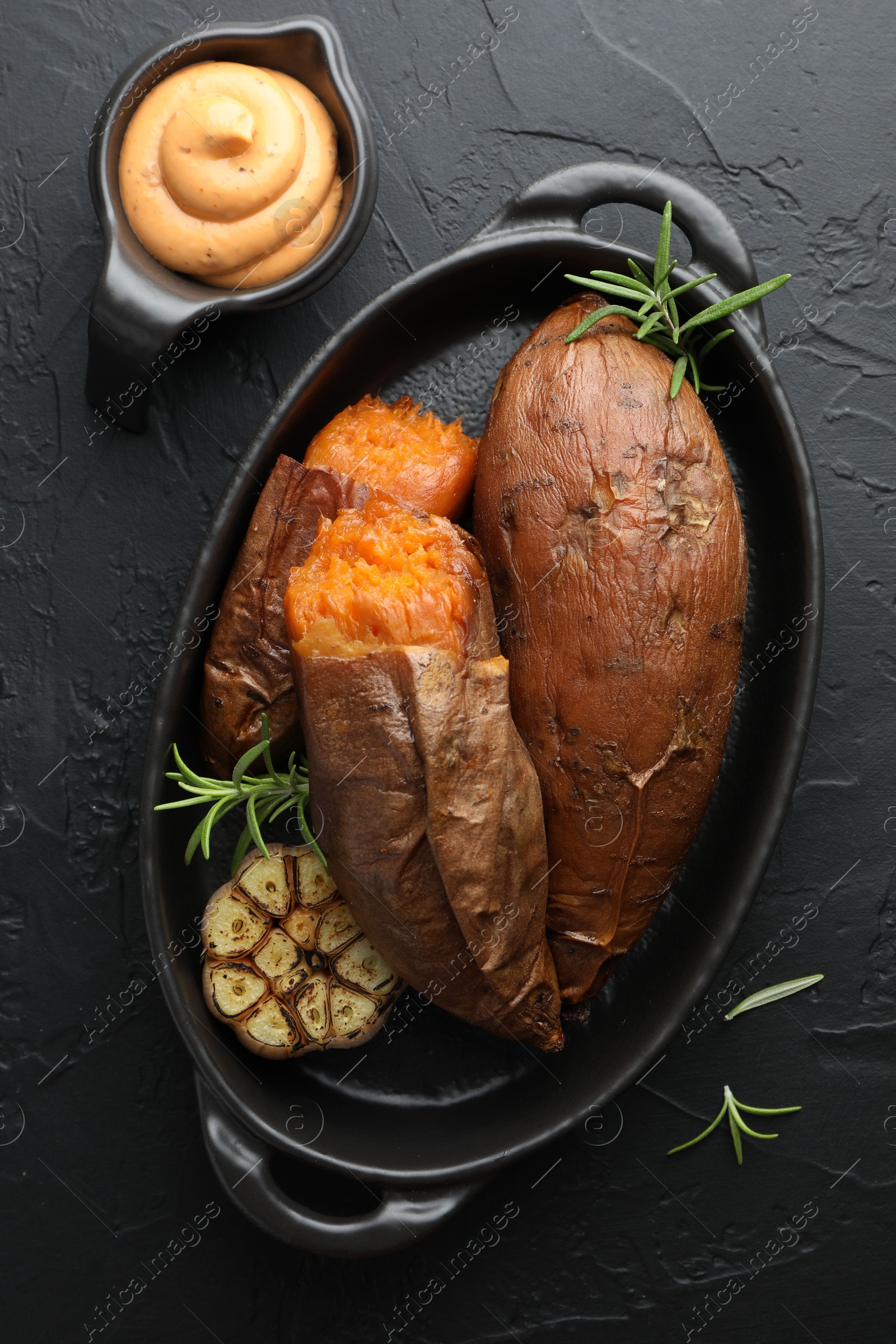 Photo of Tasty cooked sweet potatoes served with rosemary and sauce on black table, top view