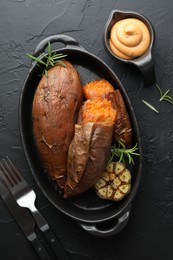 Photo of Tasty cooked sweet potatoes served with rosemary and sauce on black table, top view