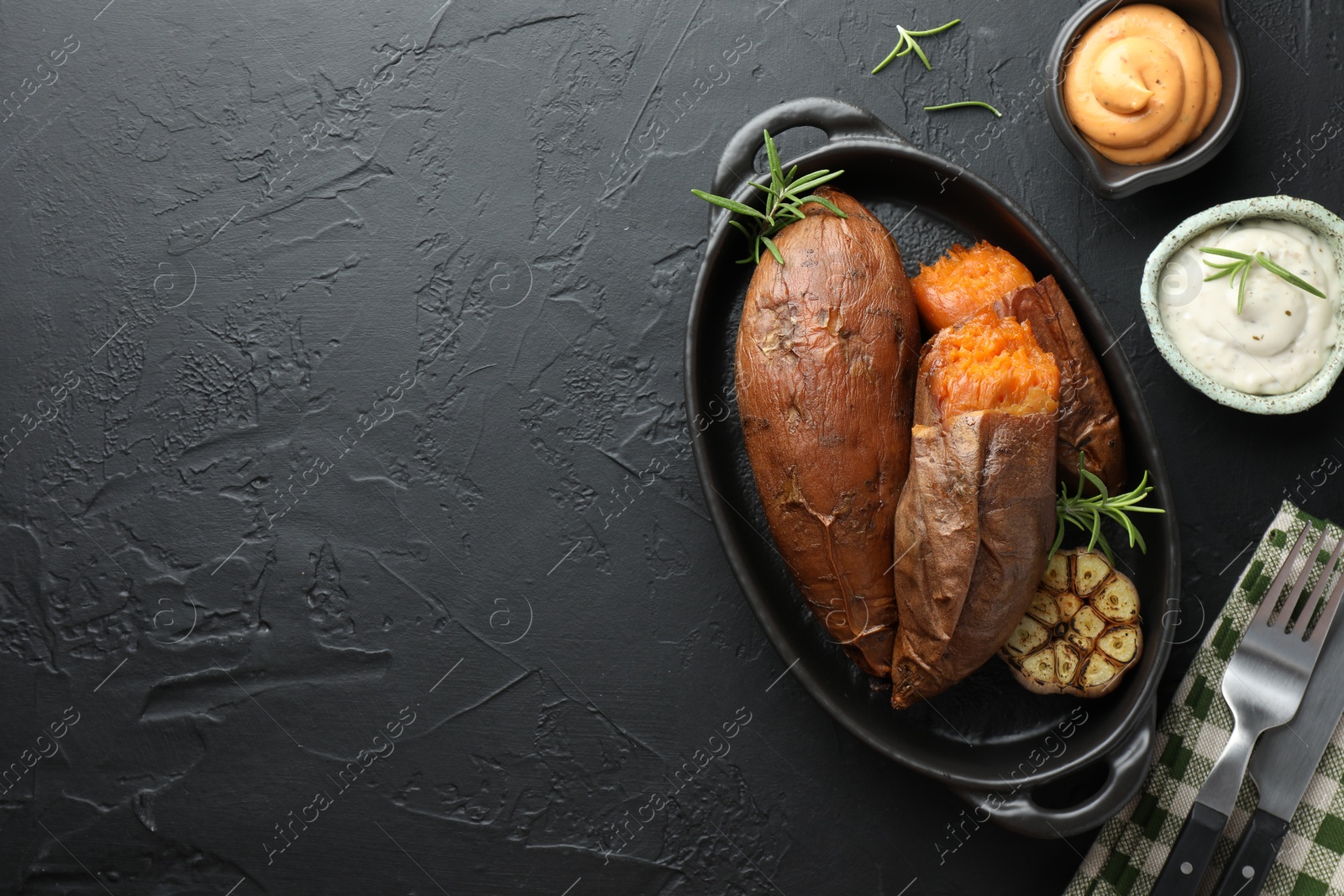 Photo of Tasty cooked sweet potatoes served with rosemary and sauces on black table, top view. Space for text