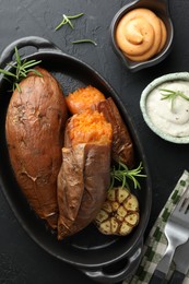 Photo of Tasty cooked sweet potatoes served with rosemary and sauces on black table, top view