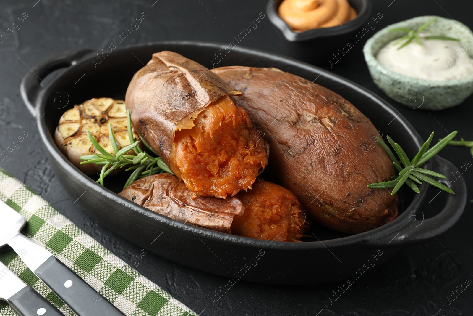 Photo of Tasty cooked sweet potatoes served with rosemary and sauces on black table, closeup