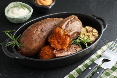 Photo of Tasty cooked sweet potatoes served with rosemary and sauces on black table, closeup