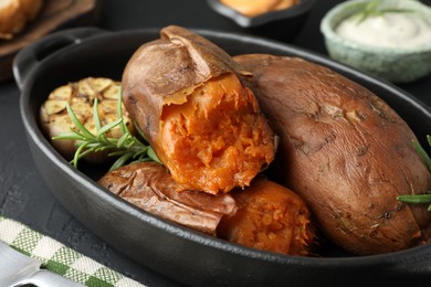 Photo of Tasty cooked sweet potatoes, rosemary and garlic on black table, closeup