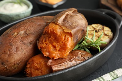 Photo of Tasty cooked sweet potatoes, rosemary and garlic on black table, closeup