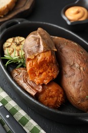 Photo of Tasty cooked sweet potatoes, rosemary and garlic on black table, closeup