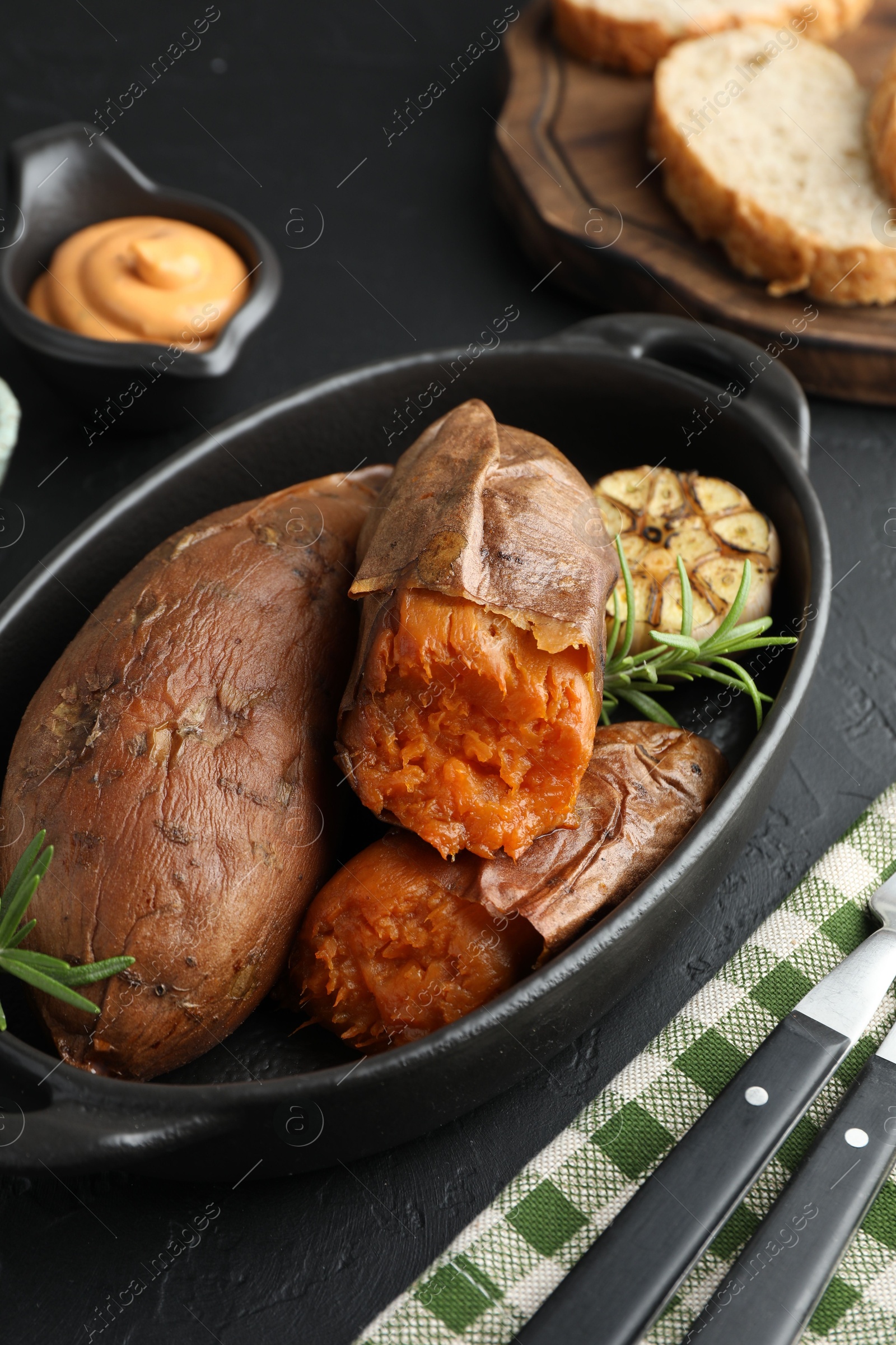 Photo of Tasty cooked sweet potatoes served with rosemary and sauce on black table, closeup