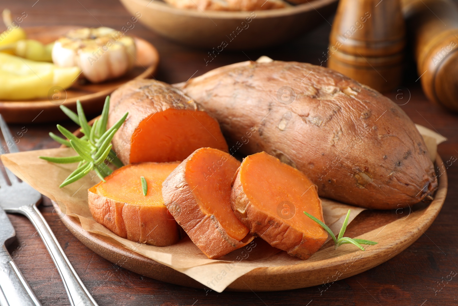 Photo of Tasty cooked sweet potatoes served with rosemary on wooden table, closeup