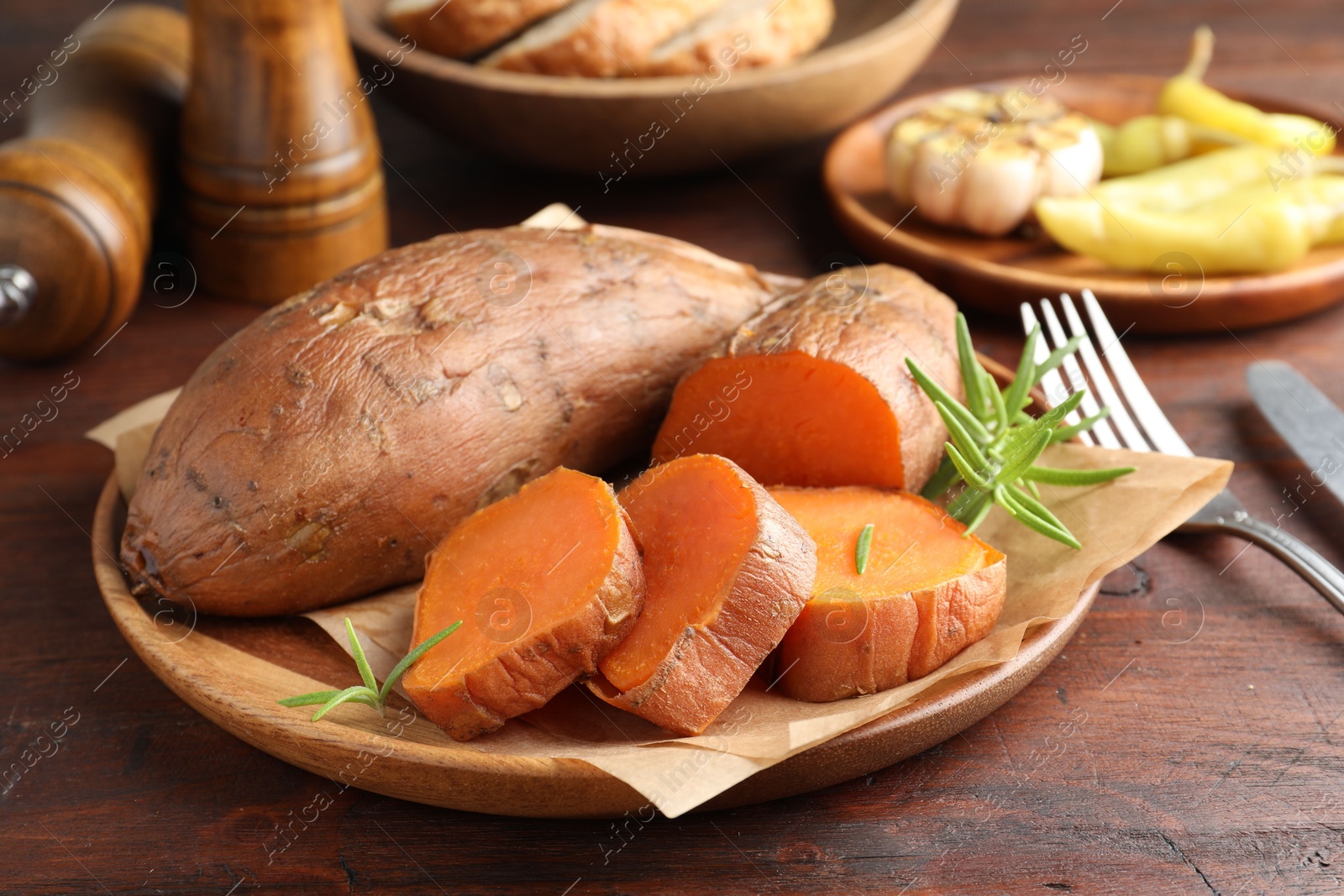 Photo of Tasty cooked sweet potatoes served with rosemary on wooden table, closeup