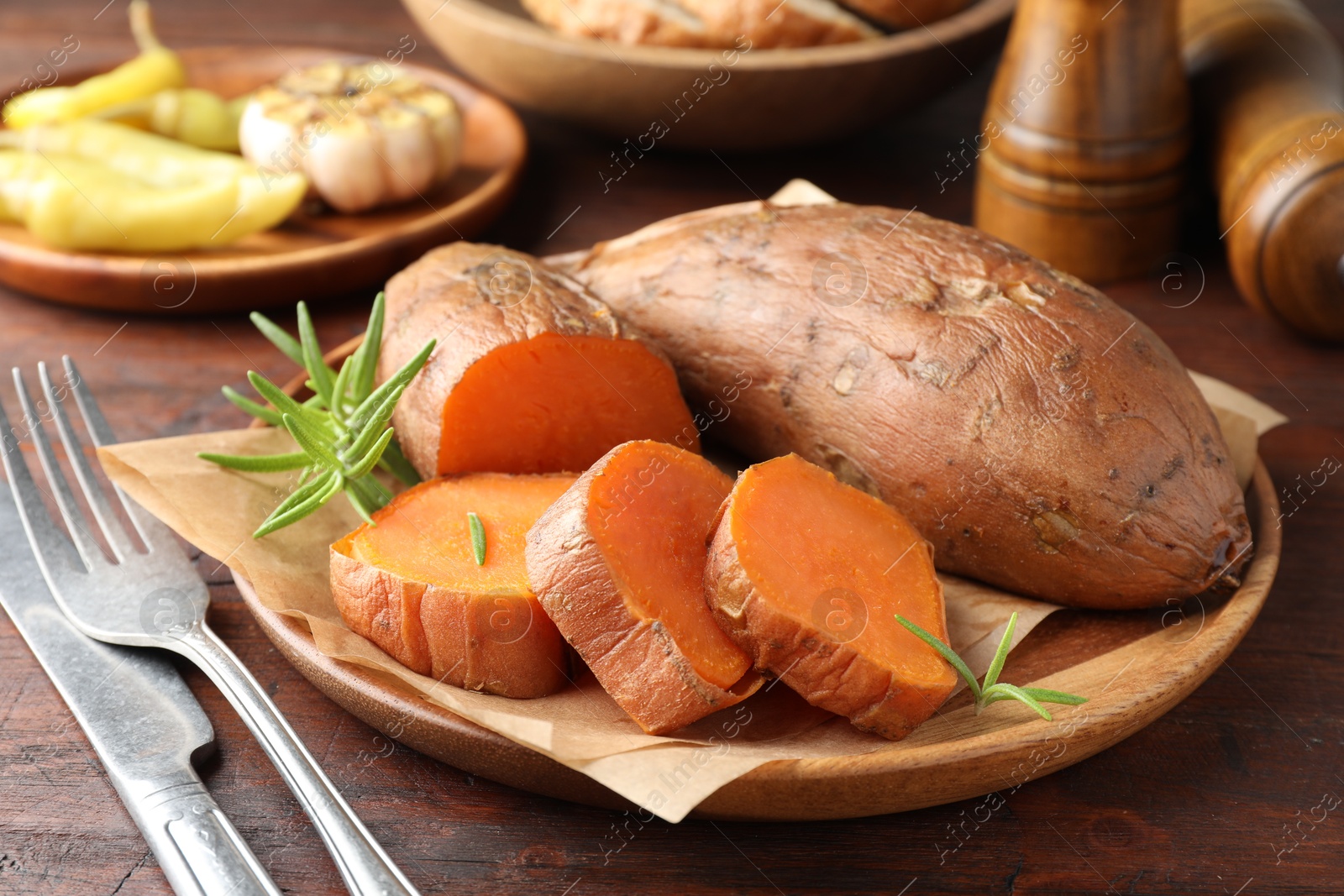 Photo of Tasty cooked sweet potatoes served with rosemary on wooden table, closeup