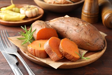 Photo of Tasty cooked sweet potatoes served with rosemary on wooden table, closeup