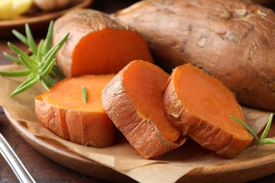 Photo of Tasty cooked sweet potatoes and rosemary on table, closeup