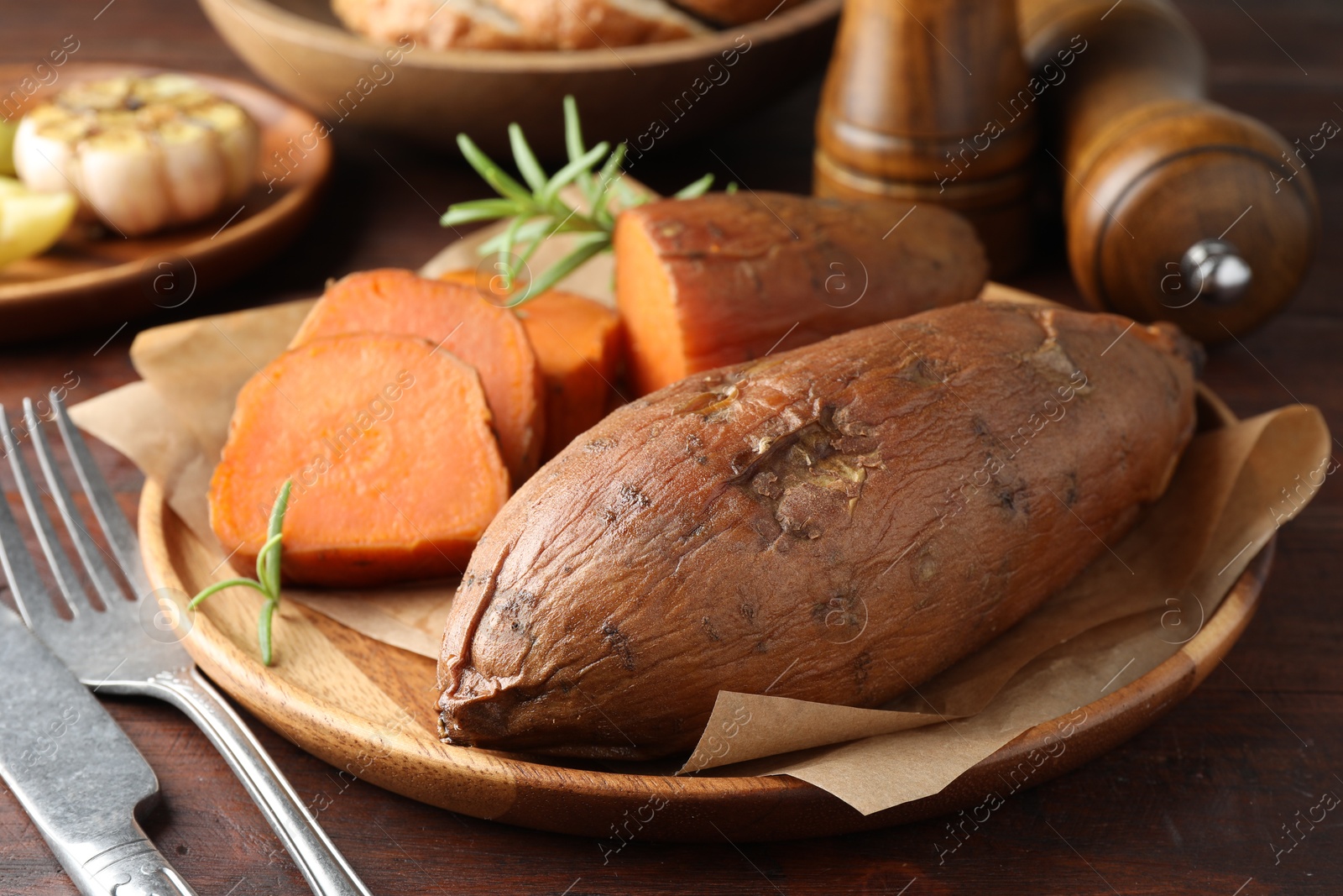 Photo of Tasty cooked sweet potatoes served with rosemary on wooden table, closeup