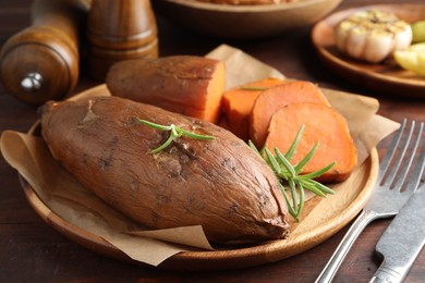 Photo of Tasty cooked sweet potatoes served with rosemary on wooden table, closeup