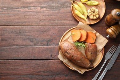 Photo of Tasty cooked sweet potatoes served with rosemary on wooden table, top view. Space for text