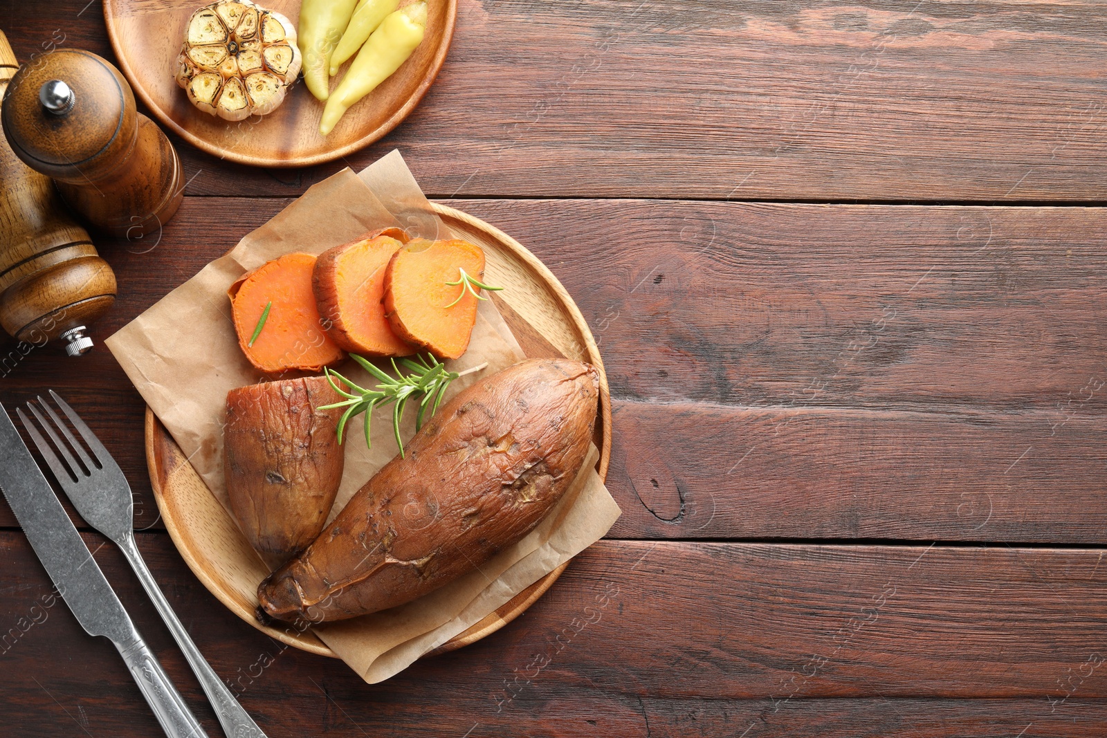 Photo of Tasty cooked sweet potatoes served with rosemary on wooden table, top view. Space for text