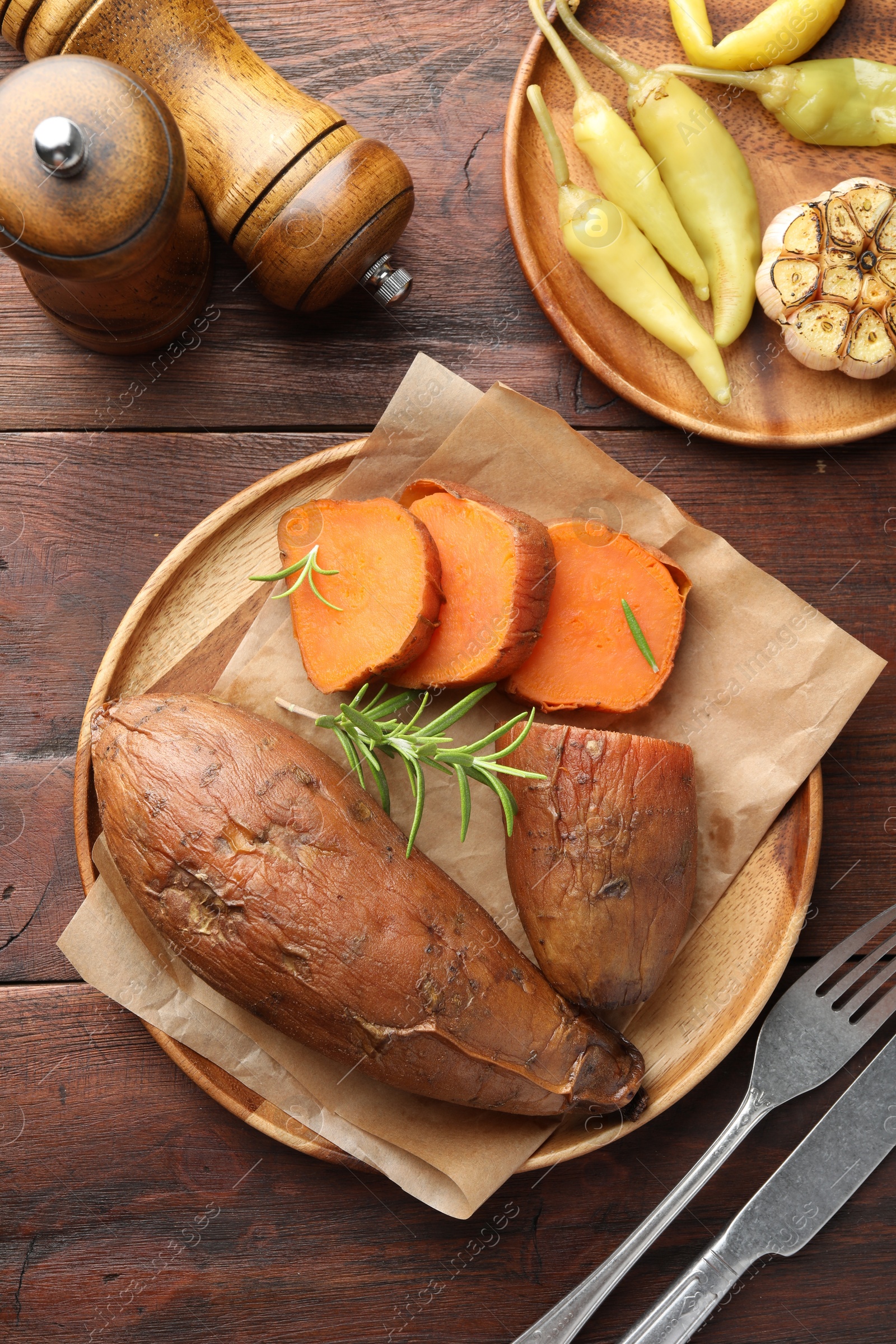 Photo of Tasty cooked sweet potatoes served with rosemary on wooden table, top view