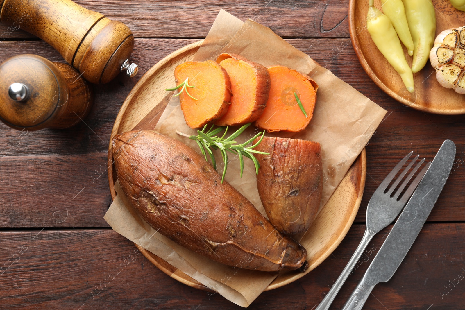 Photo of Tasty cooked sweet potatoes served with rosemary on wooden table, top view